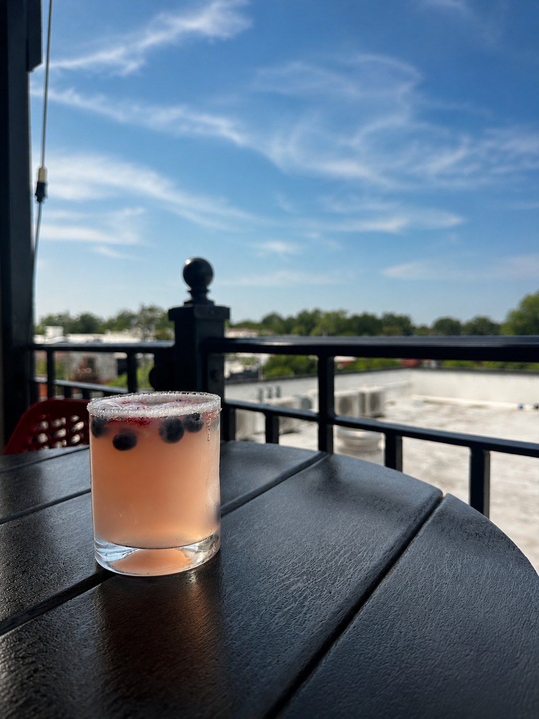 A berry cocktail with a sugared rim on a rooftop table, the rail and downtown Hartsville beyond