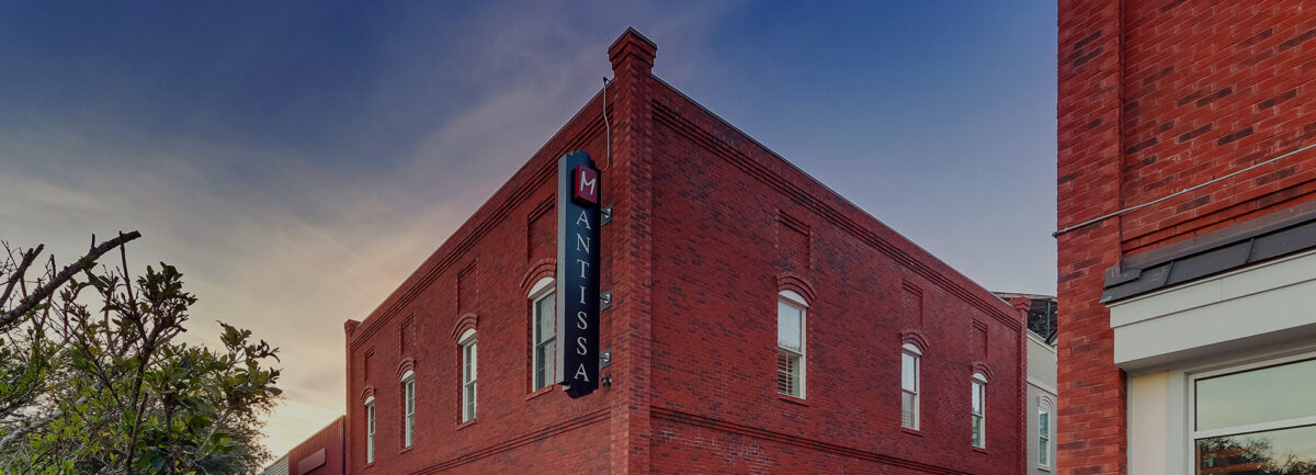 The Mantissa's restored brick corner at dusk, its vertical sign facing East Carolina Avenue