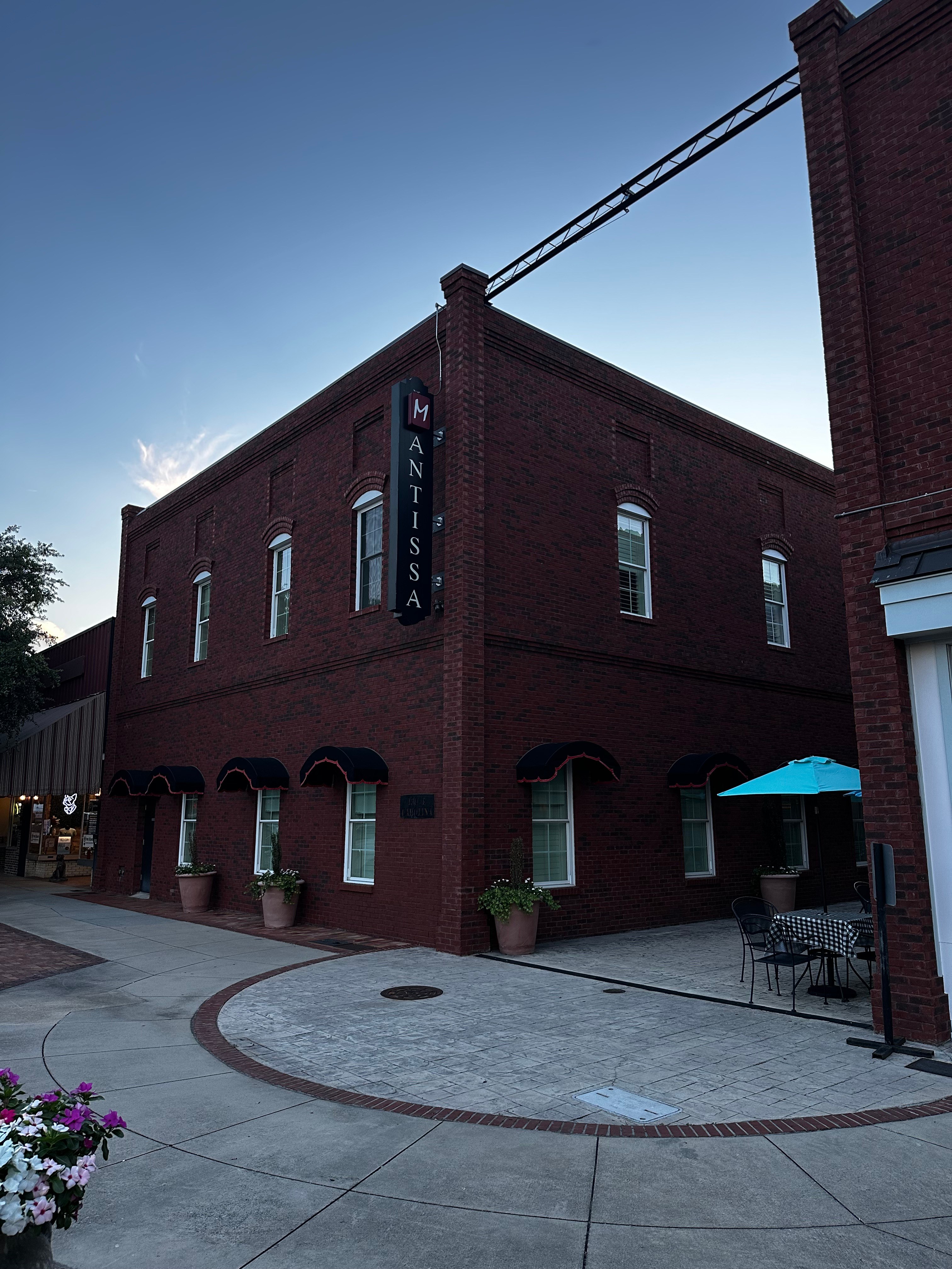 The Mantissa's brick corner at dusk, sign glowing above East Carolina Avenue
