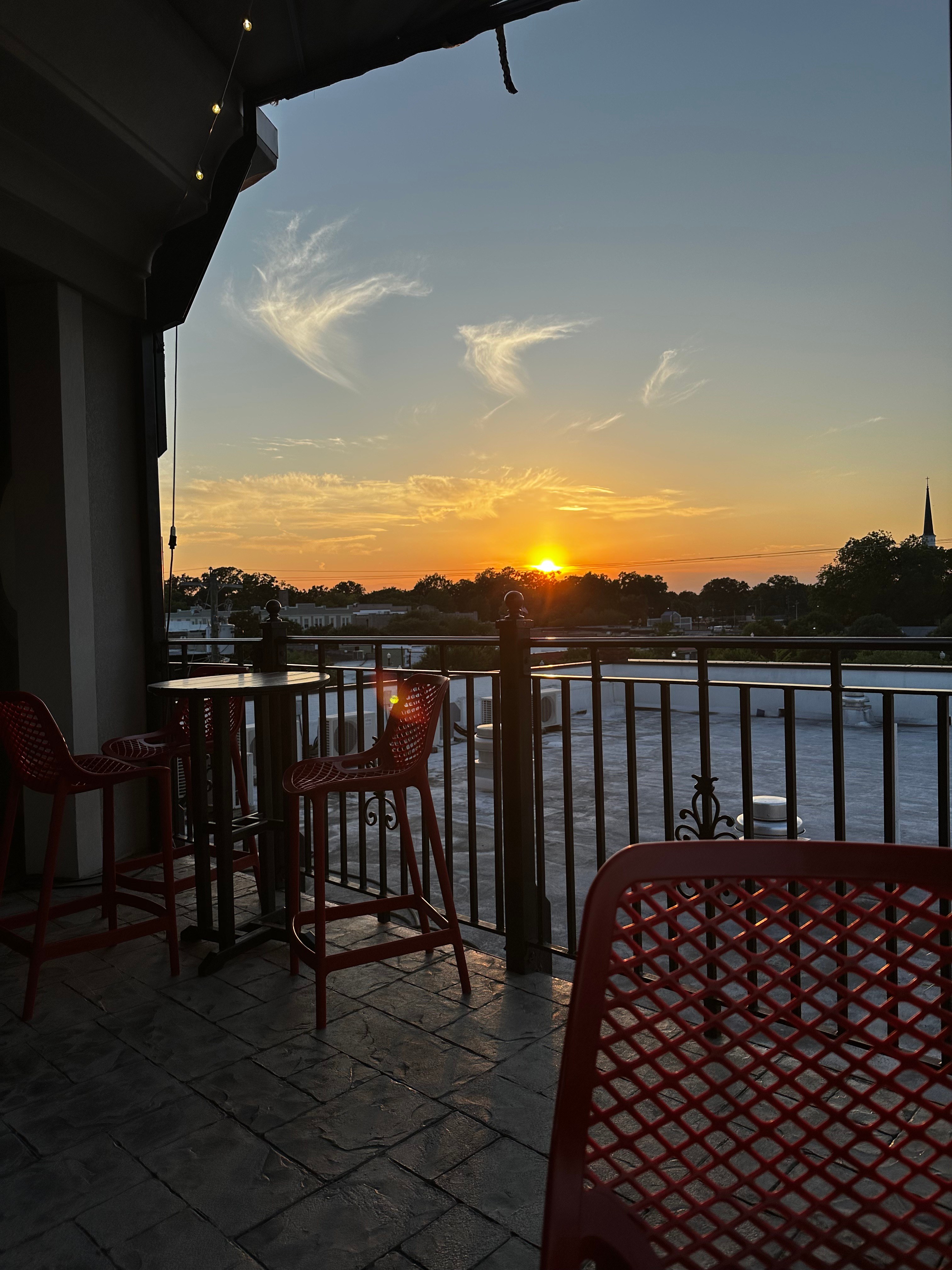 Sunset from The Rooftop's rail, red bar stools and string lights as the sun drops behind downtown Hartsville