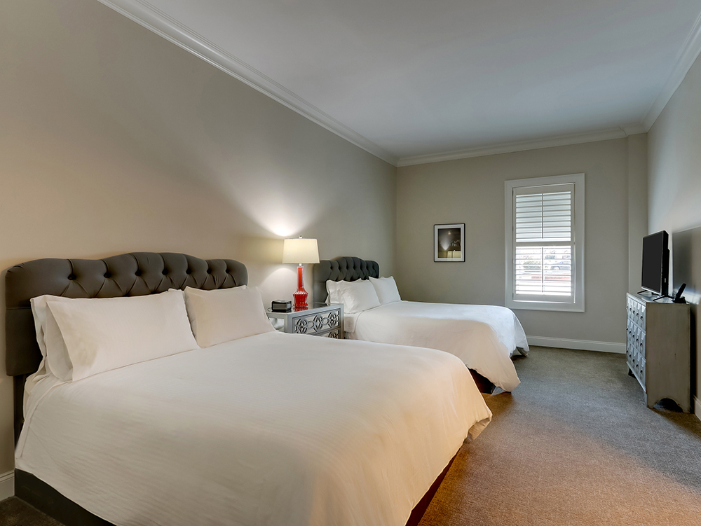 The Classic Dual Queen suite, two queen beds with a kitchen island and tall street-facing windows.