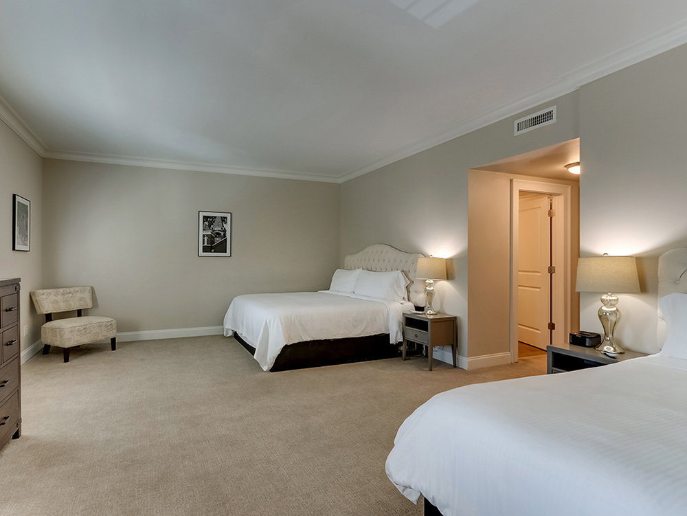 The Deluxe Dual Queen suite, two queen beds dressed in white linen with the kitchen visible beyond.