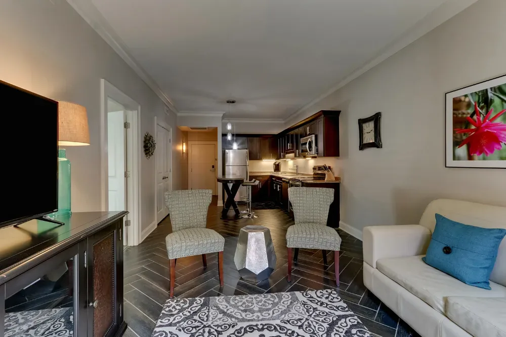 The living area of the Balcony King, a white sofa and two armchairs on a patterned rug with the kitchen at the far end.