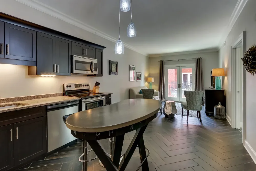 The Balcony King's full kitchen, dark cabinets and stainless appliances, with a high-top table under pendant lights and the balcony doors beyond.