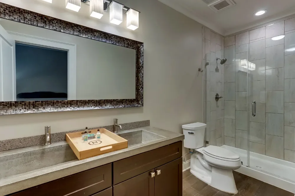 The bath of the Classic Dual Queen, a granite double vanity under a long framed mirror beside the glass shower.