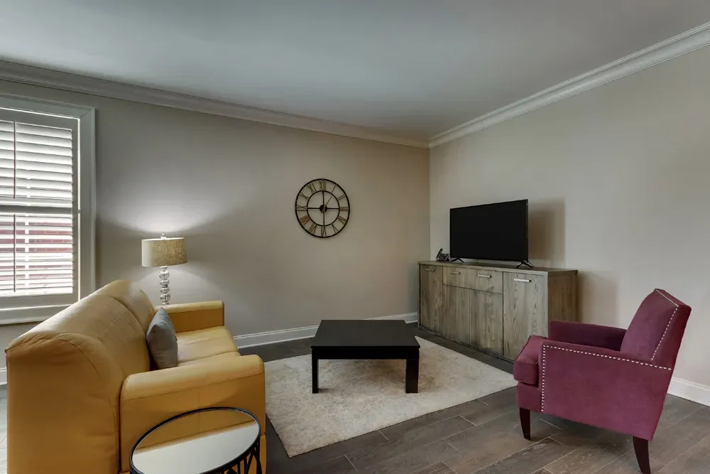 The sitting area of the Deluxe King, a yellow loveseat and plum velvet armchair around a coffee table facing the television.