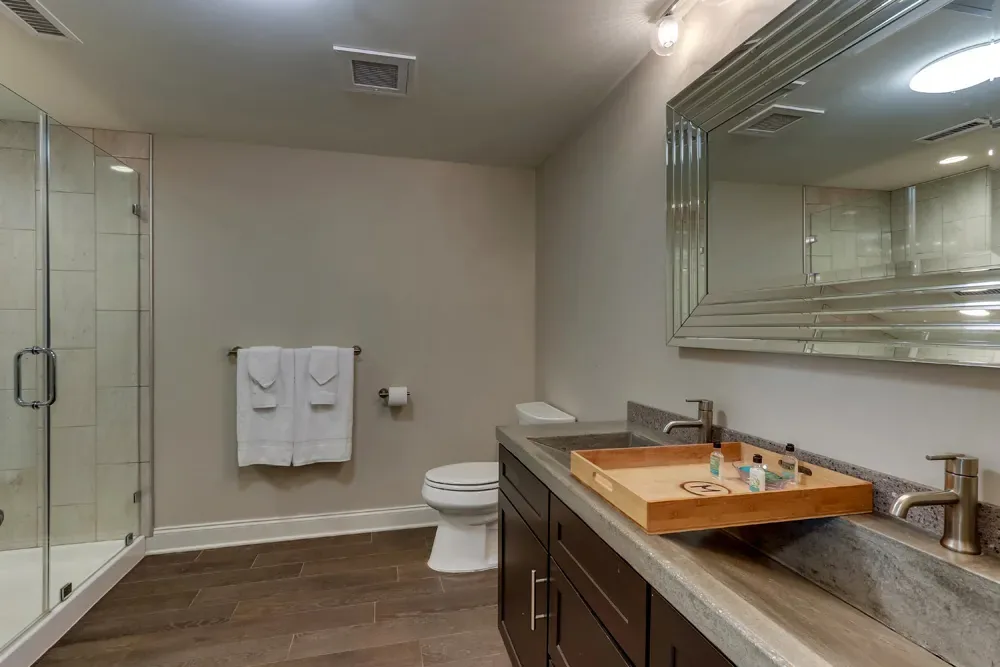 The bath of the Deluxe King, a stone-topped vanity with an amenity tray beside the glass shower.