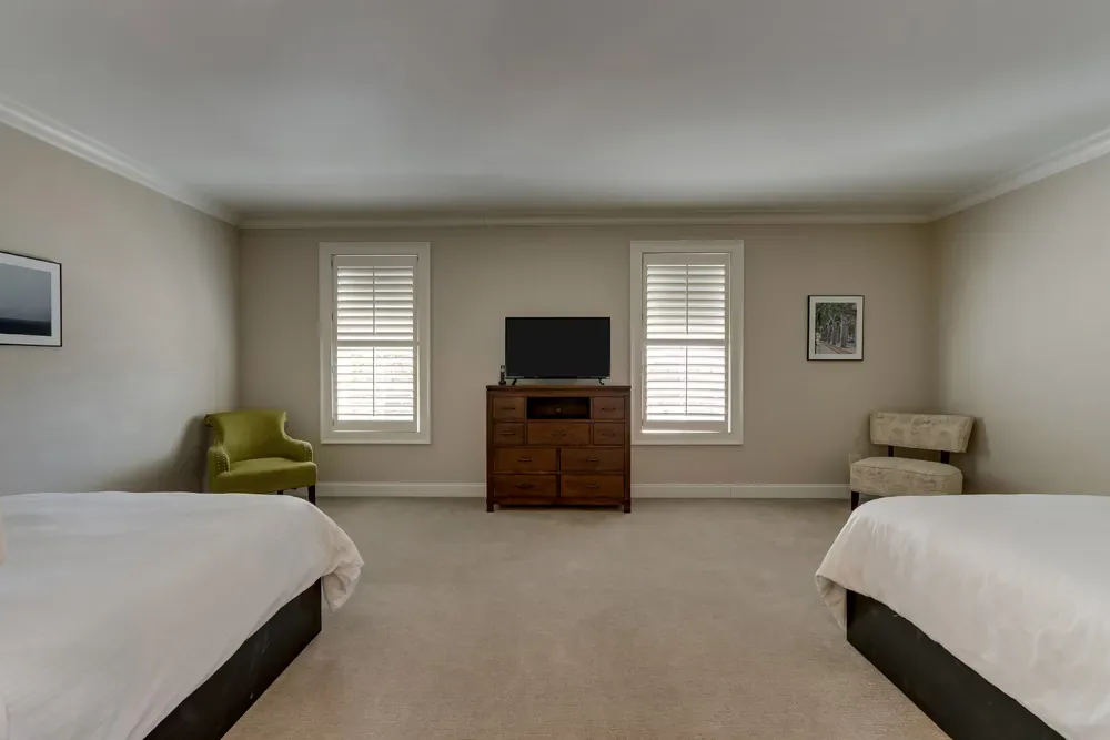 The two queen beds of the Deluxe Dual Queen facing the television console between two shuttered windows.