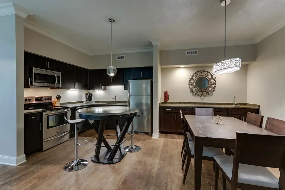 The Deluxe Dual Queen's full kitchen and dining table under pendant lights, with a stainless refrigerator and gas range.